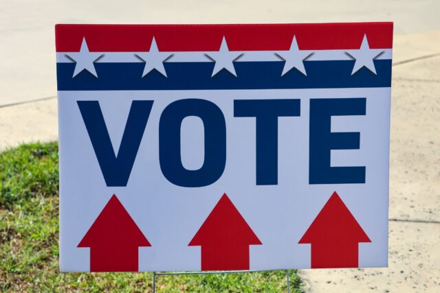 A “vote” sign with stars, stripes, and directional arrows to indicate where to go to vote or turn in ballots.