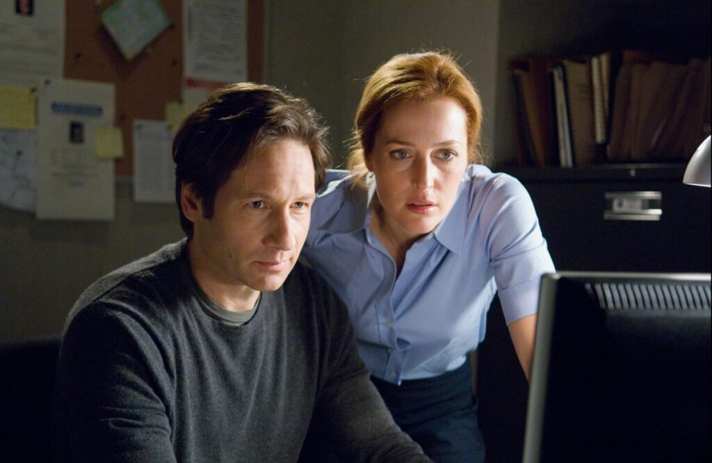 dark haired man in v-neck sweater and red haired woman in blue polo shirt looking at a computer screen