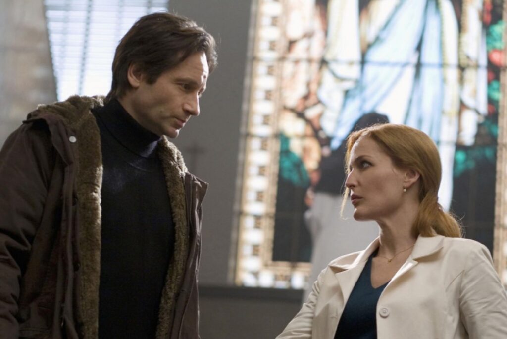 Mulder and Scully looking at each other in front of a stained glass window