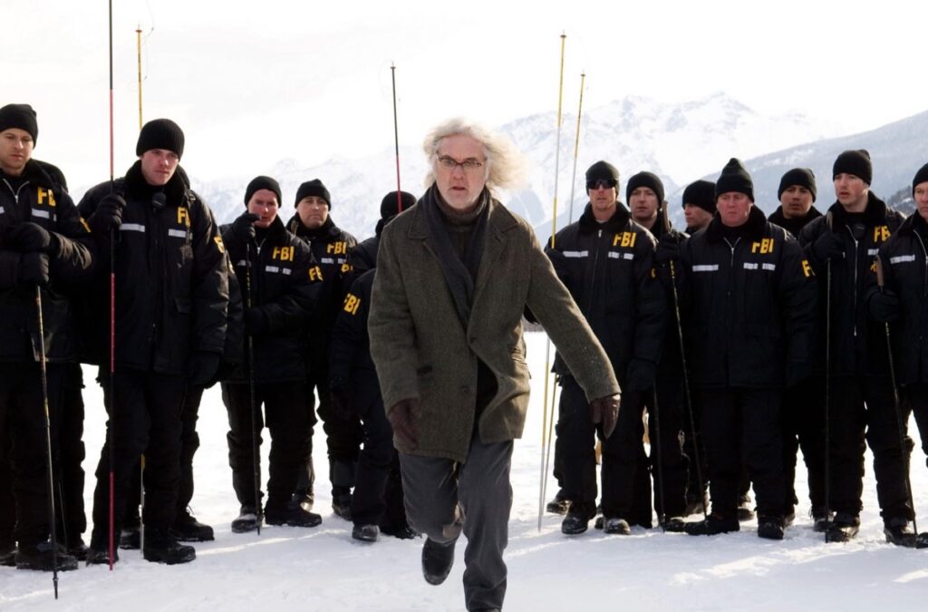older man with glasses and wild gray hair running across the snow in front of a line of armed FBI agents