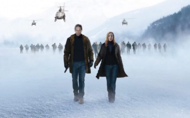 man and red-haired woman walking across a snowy surface with helicopters hovering in the background. A blood-red X stains the snow