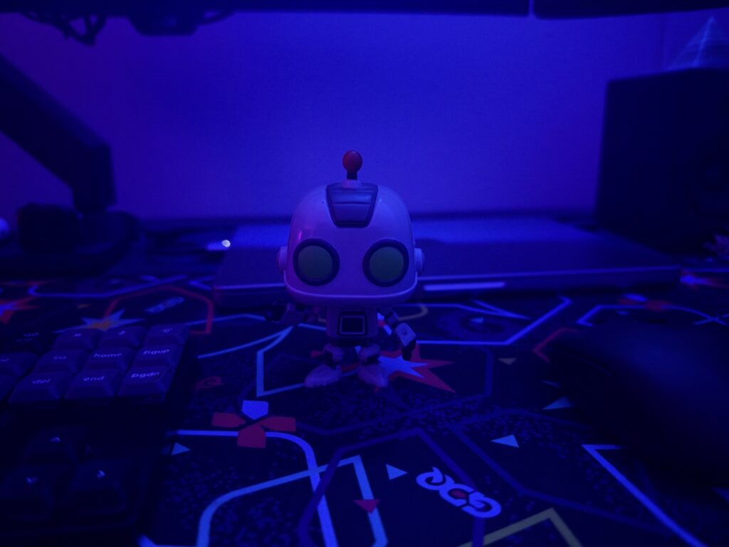 A robot figurine on a desk mat in front of a MacBook Pro