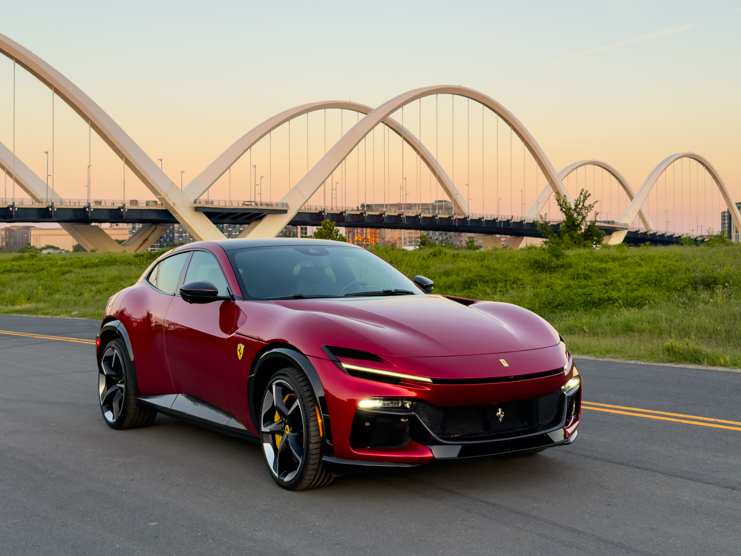 A red Ferrari Purosangue at dawn with a bridge in the background.