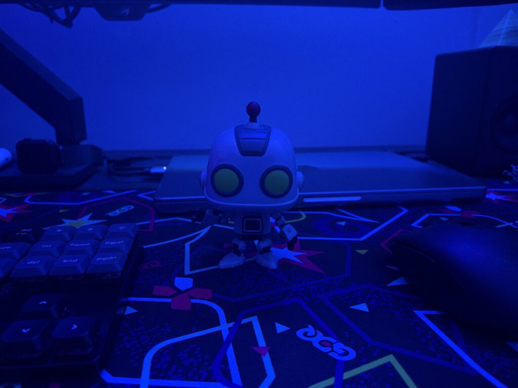 A robot figurine on a desk mat in front of a MacBook Pro