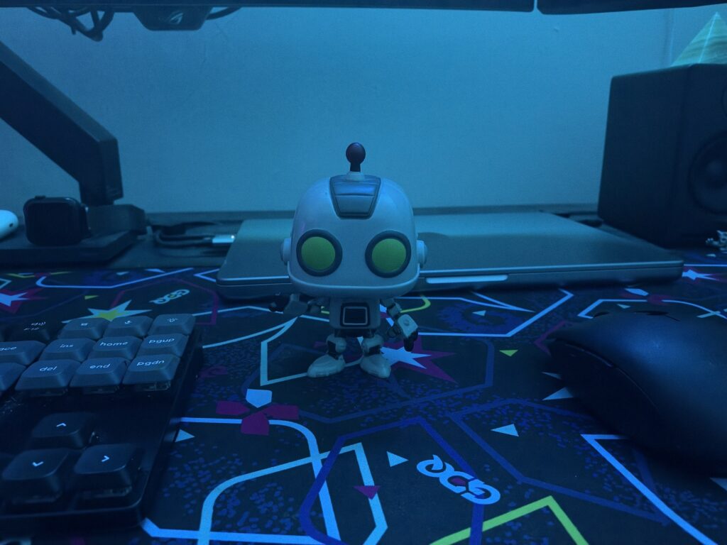 A robot figurine on a desk mat in front of a MacBook Pro