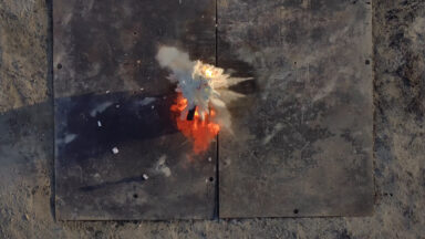 Fire retardant balls dropped by Anduril's Ghost-X drone explode on a fire in a test. The scene from above shows a cloud of fire retardant just spreading out with the blaze beneath it.