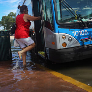 Image of a person boarding a bus that's stopped in ankle-deep water.