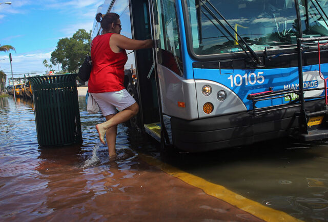 Image of a person boarding a bus that's stopped in ankle-deep water.