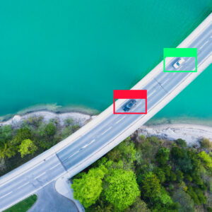 two cars drive on a bridge, seen from above. One is bounded by a green box, one by a red box