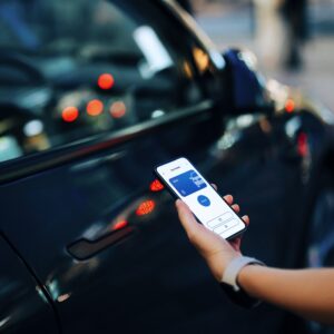 Cropped shot of a female hand using mobile app device on smartphone to unlock the doors of her intelligence car in car park. Wireless and modern technology. Smart car with digital car key concepts