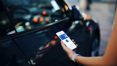 Cropped shot of a female hand using mobile app device on smartphone to unlock the doors of her intelligence car in car park. Wireless and modern technology. Smart car with digital car key concepts