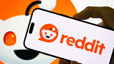 In this photo illustration, a person holds a smartphone displaying the logo of Reddit Inc.