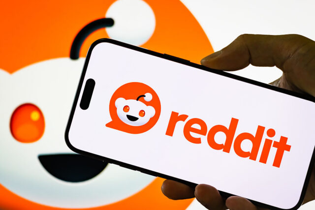 In this photo illustration, a person holds a smartphone displaying the logo of Reddit Inc.