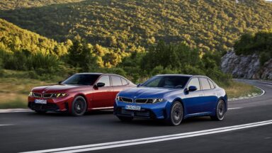 A red and a blue BMW 3 series drive along a road