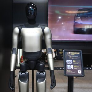 Tesla's Optimus Gen-3 humanoid robot at an exhibition in Hangzhou, Zhejiang Province, China on September 23, 2026. The robot is standing in front of a screen displaying a car.