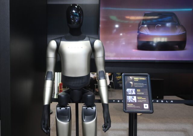 Tesla's Optimus Gen-3 humanoid robot at an exhibition in Hangzhou, Zhejiang Province, China on September 23, 2026. The robot is standing in front of a screen displaying a car.