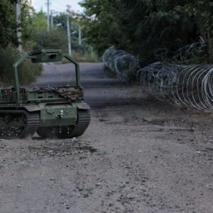 A ground robotic system drives along a road, delivering supplies on September 4, 2026 in Druzhkivka, Donetsk Oblast, Ukraine. The tracked robot vehicle is seen on a gravel and dirt road lined with coils of barbed wire.
