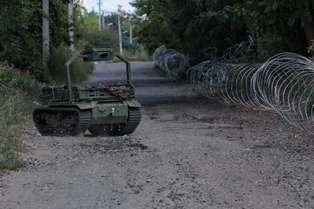 A ground robotic system drives along a road, delivering supplies on September 4, 2026 in Druzhkivka, Donetsk Oblast, Ukraine. The tracked robot vehicle is seen on a gravel and dirt road lined with coils of barbed wire.