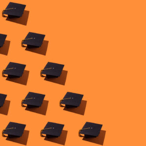 Pattern of black graduation caps with gold tassel with hard shadow, on the left side, on orange background