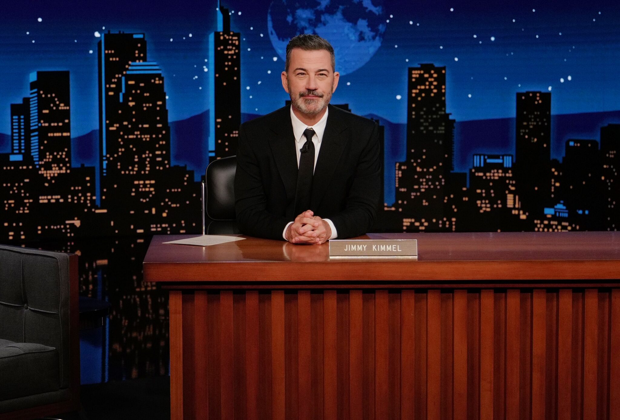 ABC host Jimmy Kimmel sitting at his desk on the set of his show.