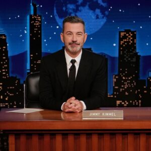 ABC host Jimmy Kimmel sitting at his desk on the set of his show.