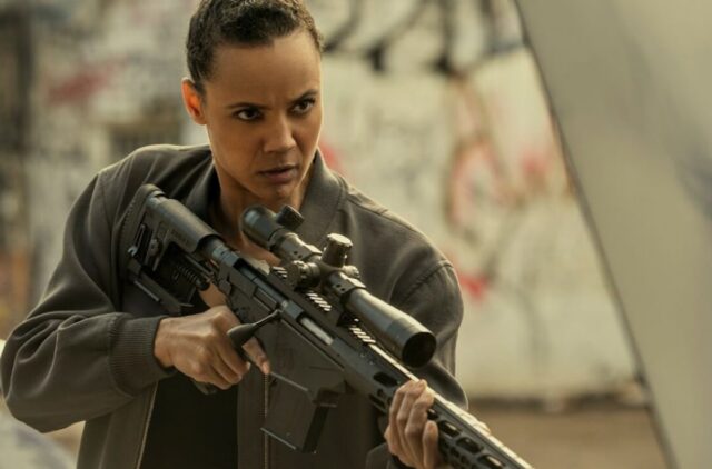 young black woman with hair pulled back in combat gear and holding a high-powered rifle in her hands