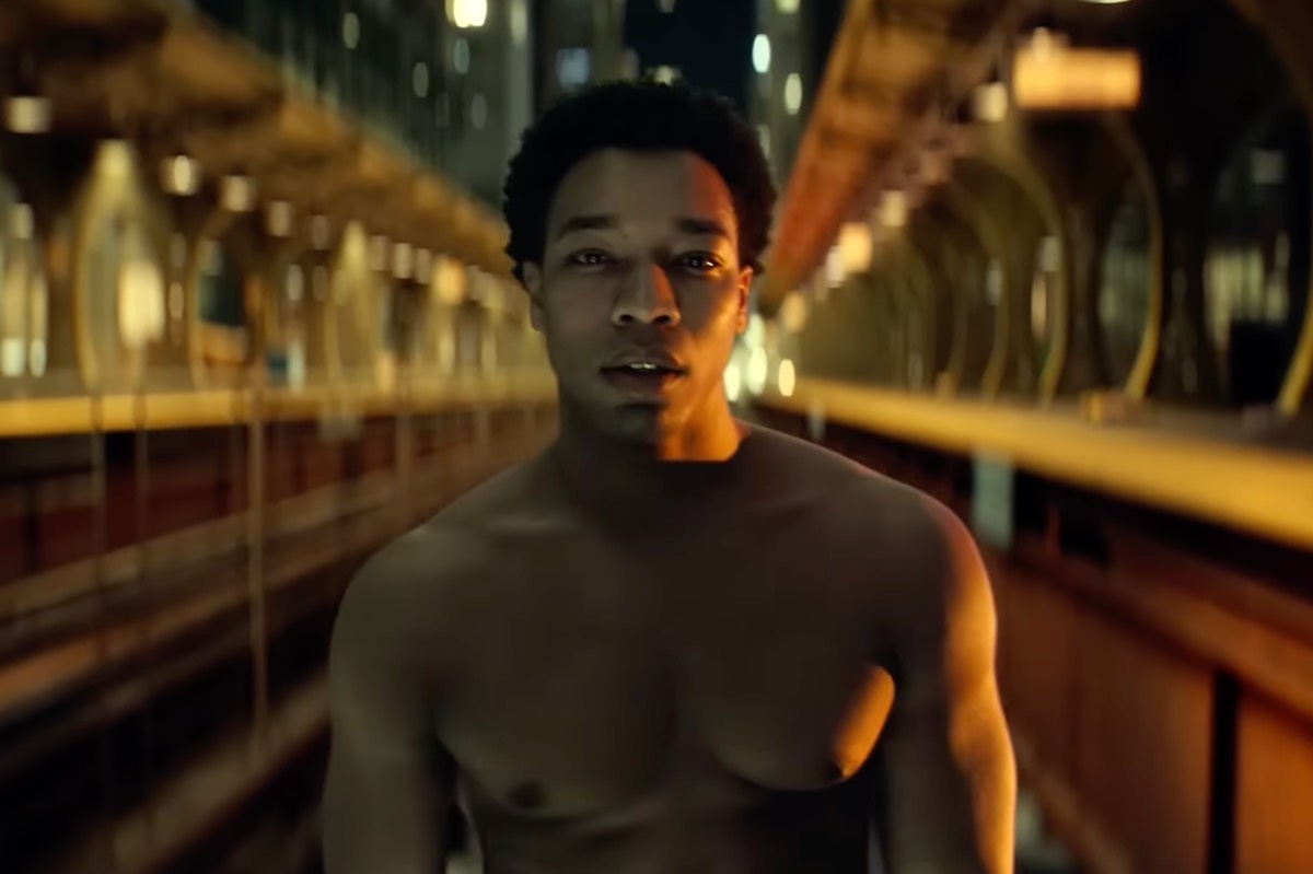 young bare chested black man walking down a L train track with a dated drugged out look on his face