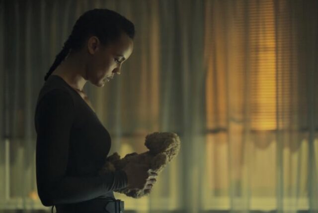 black woman looking down a stuffed animal, deep in reflection.