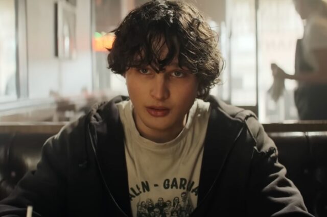 scruffy teen with tousled hair in a hoodie seated at a table in a diner