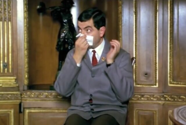 Rowan Atkinson as Mr. Bean blowing his nose discreetly while in an elegant reception area
