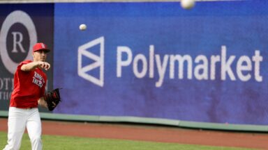 A Major League baseball player throws a ball during warmups, while a large sign advertising Polymarket is seen on the outfield wall.