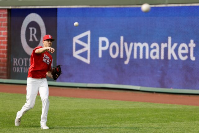 A Major League baseball player throws a ball during warmups, while a large sign advertising Polymarket is seen on the outfield wall.