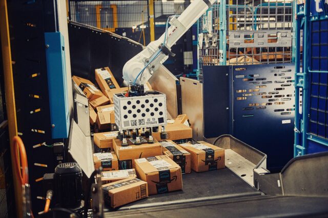 A robotic arm system called Cardinal uses a suction system to grab boxes from a pile of Amazon packages and stack them inside a rolling cart.
