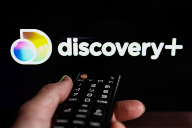 TV remote control and Discovery+ logo displayed on a laptop screen are seen in this photo.