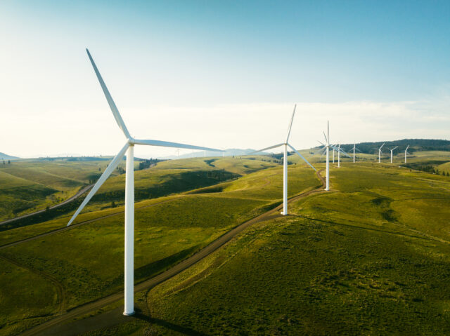 Wind turbines tower above the earth in a rural setting, drawing renewable energy as they spin. Sustainable energy and green technology that considers the environment. Shot in Washington state, USA.
