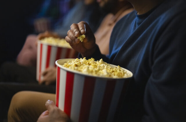 A close-up shot of a hand grabbing popcorn from a red and white striped container, symbolizing the enjoyment of a movie theater experience.