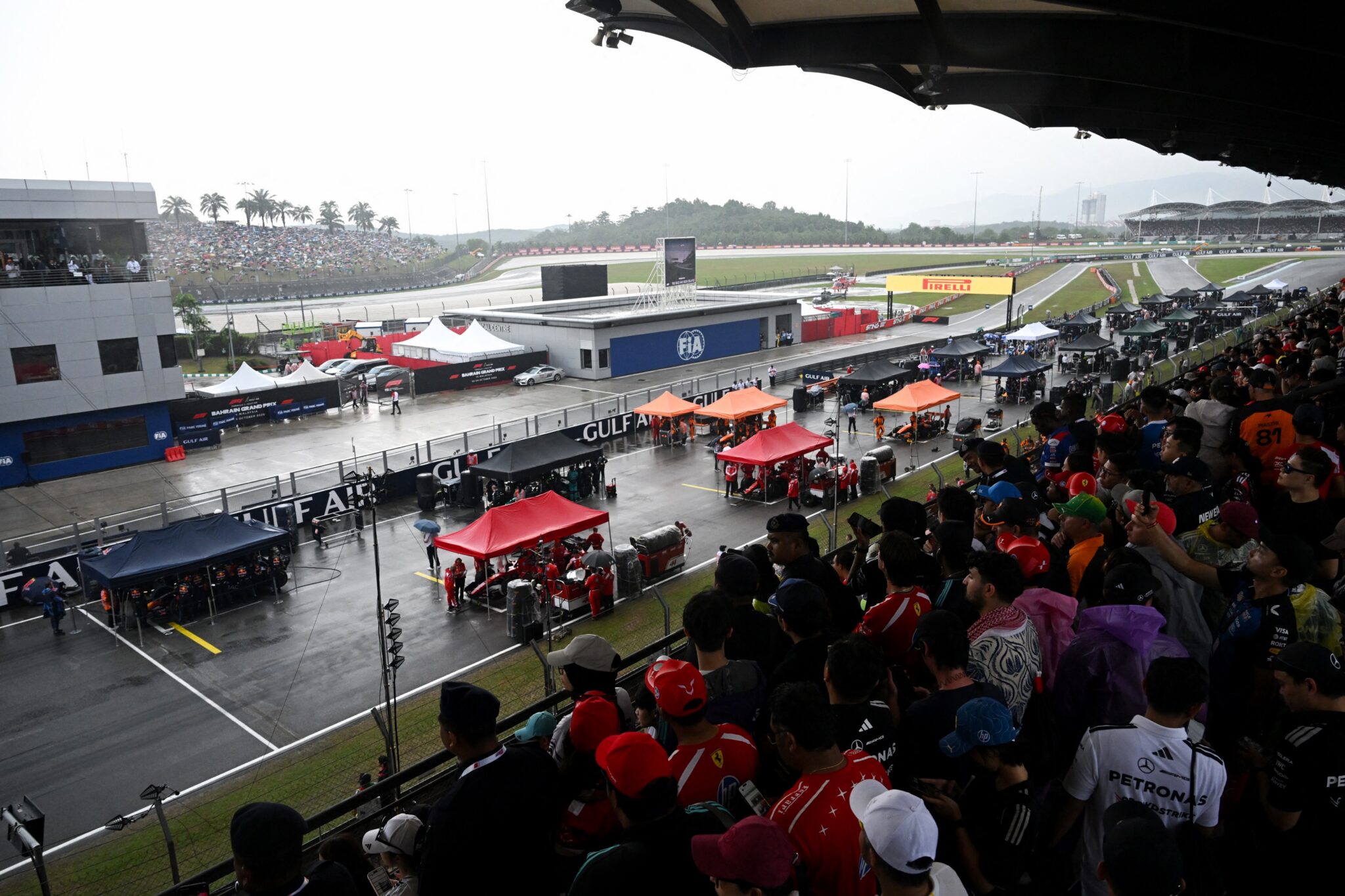Teams gather around the cars as the start of the race has been delayed due to heave rain at the Formula One Bahrain Grand Prix in Sepang on October 4, 2026. (Ph