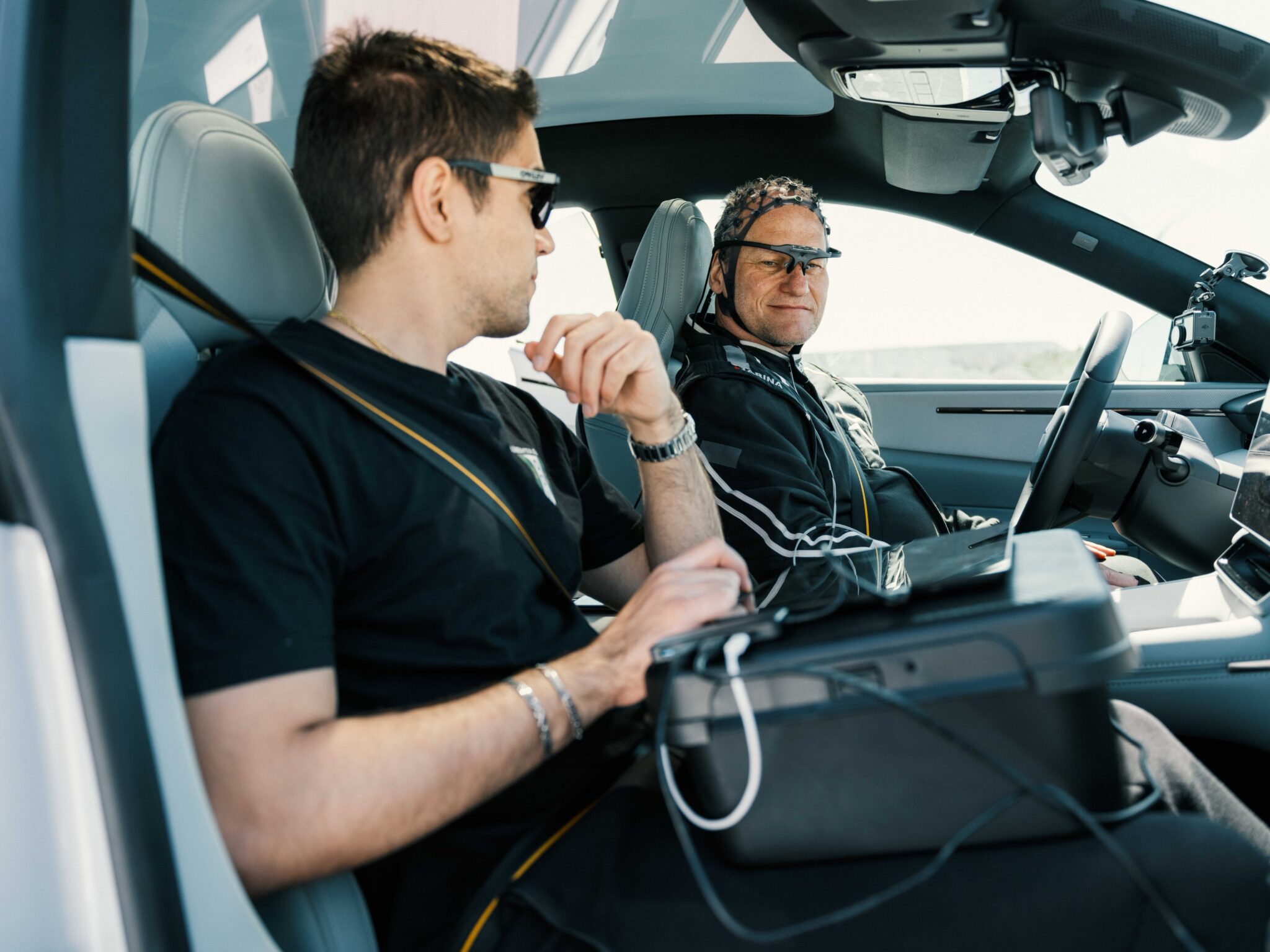 Two people sit in a car, one has electrodes all over his head
