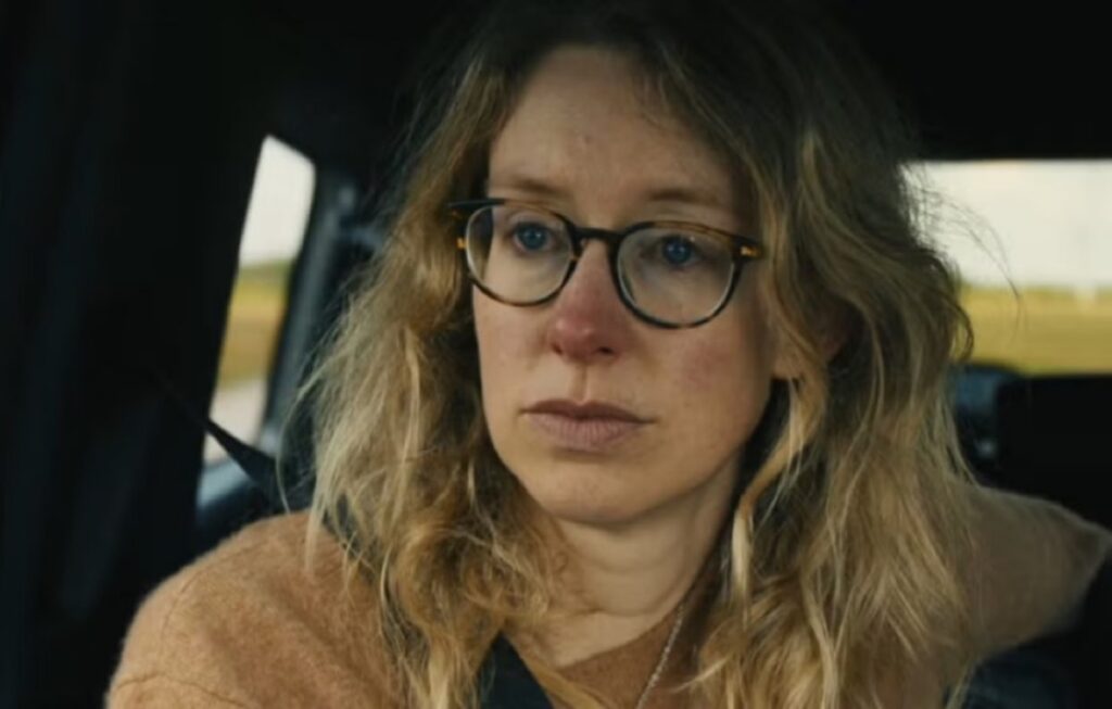 disheveled blonde woman in glasses staring out a car window