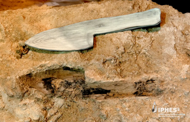 Image of a stone block with the imprint of a device with a blade and handle, with a model of a wooden version of the object that formed it just above.