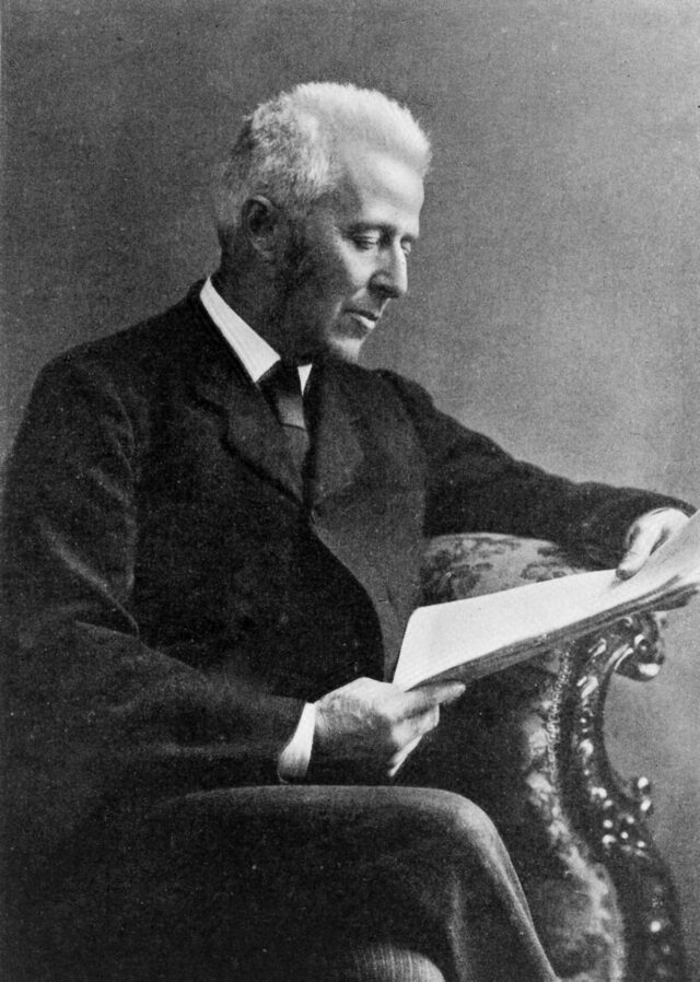 black and white photograph of a white haired man sitting and perusing a paper